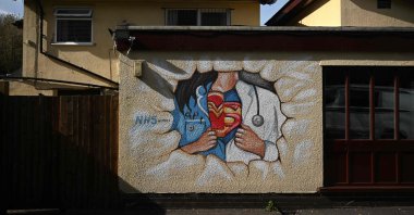 Graffiti depicts the badge of a superhero concealed under a nurse's and doctor's uniform in homage to the efforts of NHS staff during the coronavirus crisis on a wall in Pontefract, northern England, April 14, 2020. (AFP Photo)