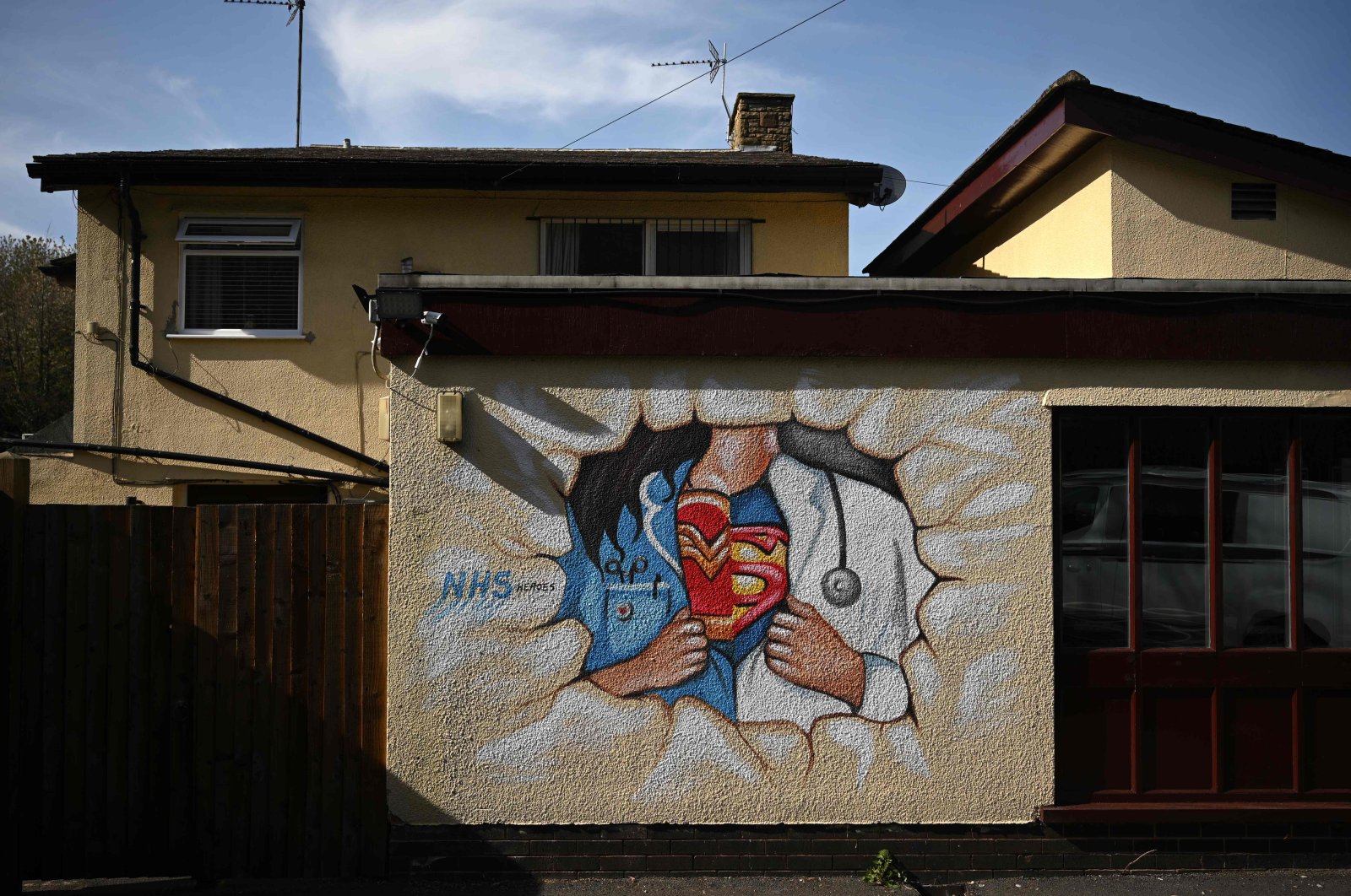 Graffiti depicts the badge of a superhero concealed under a nurse's and doctor's uniform in homage to the efforts of NHS staff during the coronavirus crisis on a wall in Pontefract, northern England, April 14, 2020. (AFP Photo)