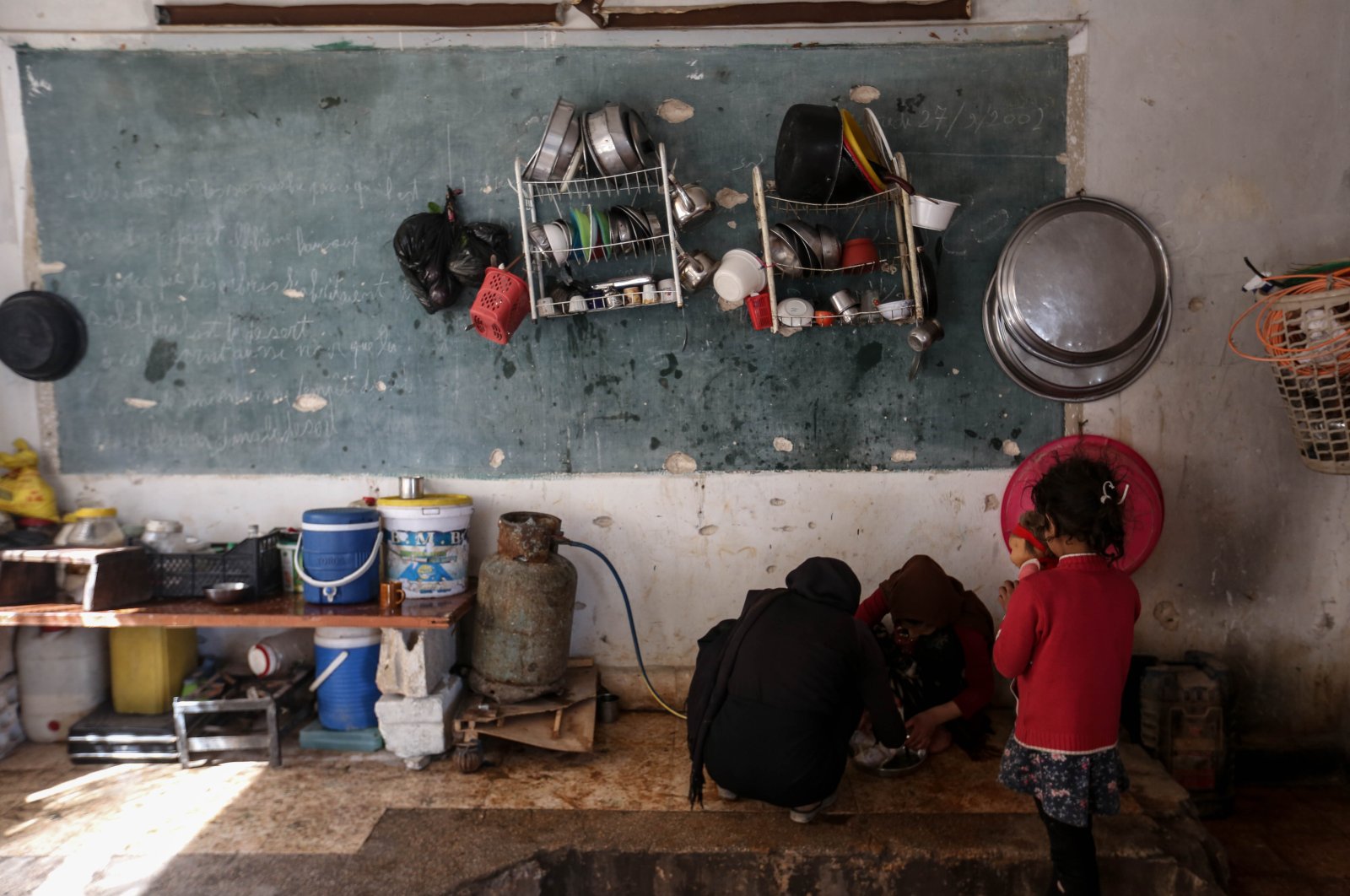 Families staying in bombed-out schools aim to transform the damaged buildings into makeshift homes by using blackboards as a place to hang clothes and turning some classrooms into kitchens, Friday, April 17, 2020. (AA)