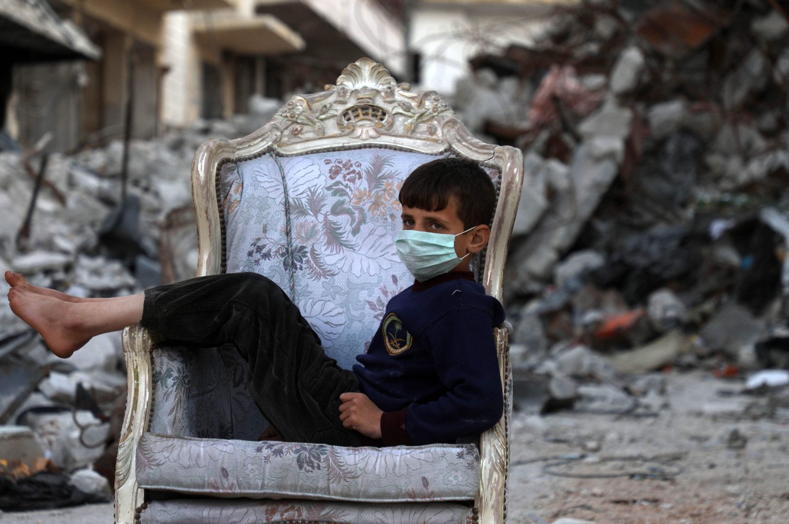 A child sits on a couch found in a street, ravaged by pro-regime forces air strikes, in the town of Ariha in the northern countryside of the Idlib province, Saturday, April 11, 2020. (AFP)
