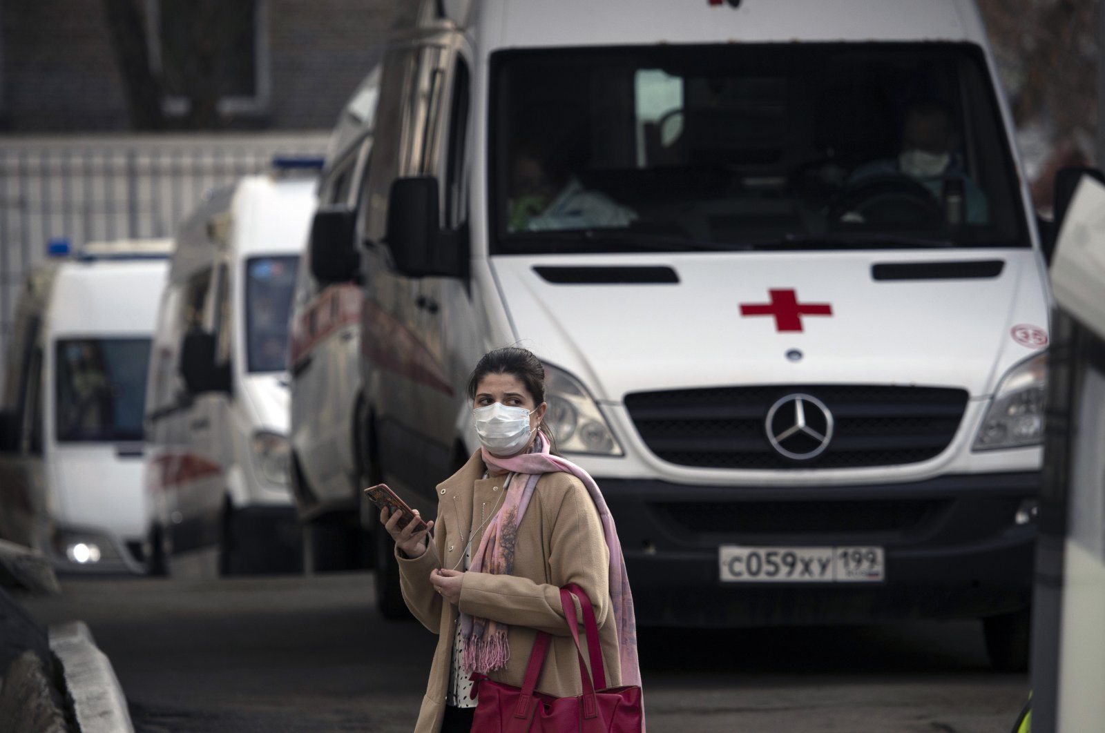 A woman wearing a face mask stands next to ambulances as they queue to transfer patients suspected of having the coronavirus infection to a hospital in Moscow, Russia, April 9, 2020. (AP Photo)