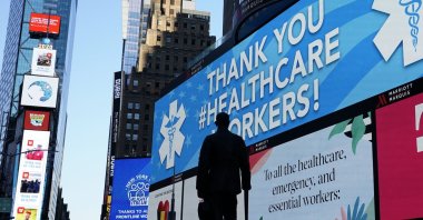 The statue of composer George M. Cohan is seen in Times Square in New York City, while in the background some of the nearly 1,800 digital billboards and screens across all five boroughs are displaying messages of public safety, gratitude, pride and solidarity with essential workers, New York, U.S., April 19, 2020. (AFP Photo)