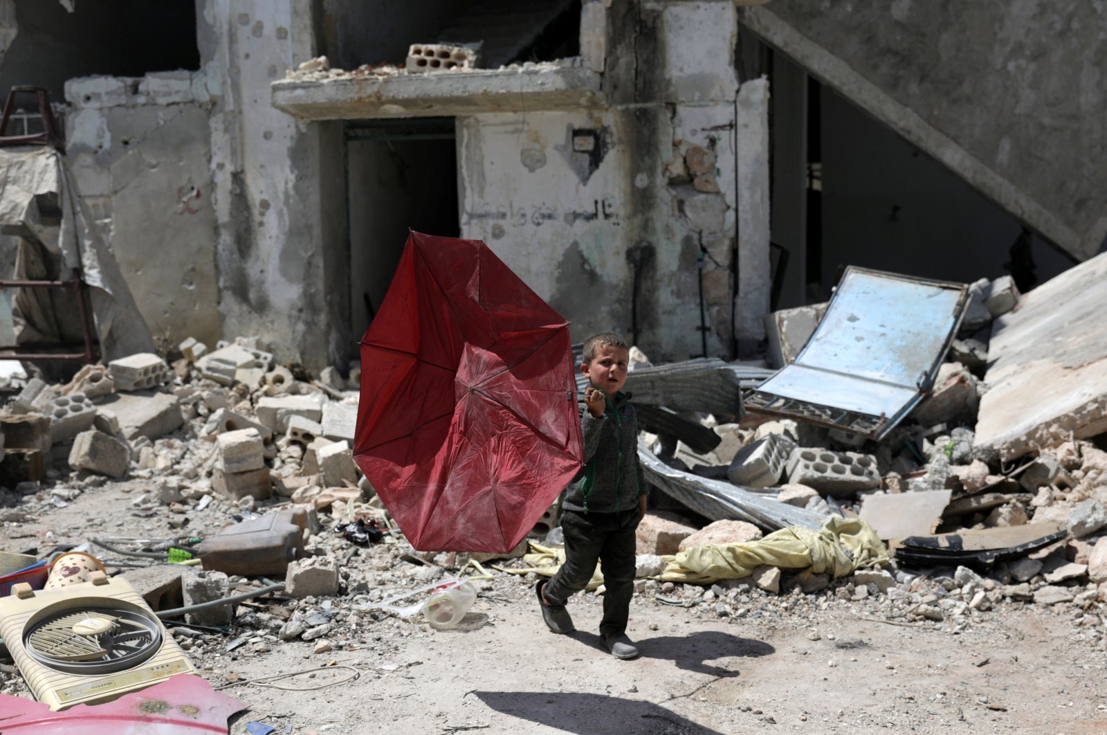 A boy carries a broken umbrella as he walks past a damaged building in the rebel-held town of Nairab, in northwest Syria's Idlib region, Syria, Friday, April 17, 2020. REUTERS