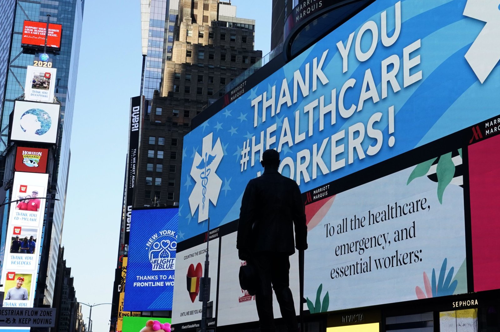 The statue of composer George M. Cohan is seen in Times Square in New York City, while in the background some of the nearly 1,800 digital billboards and screens across all five boroughs are displaying messages of public safety, gratitude, pride and solidarity with essential workers, New York, U.S., April 19, 2020. (AFP Photo)