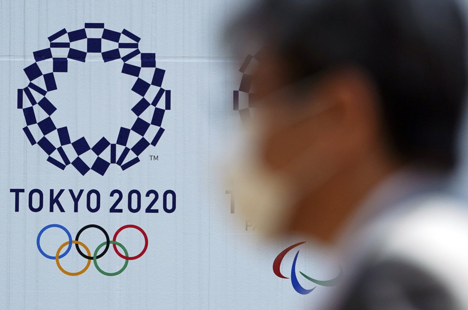 A man wearing a face mask walks near the logo of the Tokyo 2020 Olympics, in Tokyo, April 2, 2020. (AP Photo)