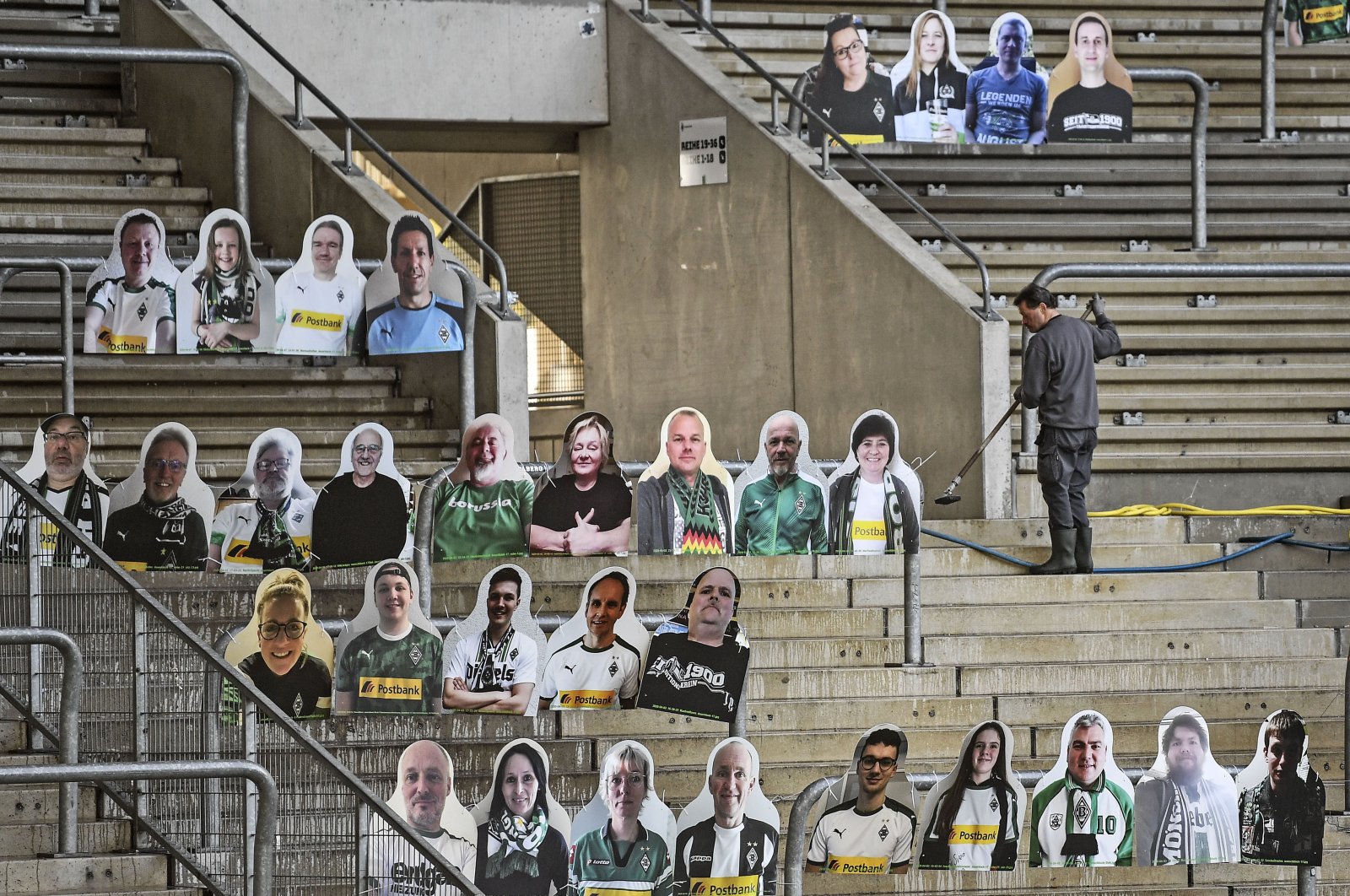 A worker cleans the supporters' tribune where portraits of fans of German Bundesliga soccer club Borussia Moenchengladbach are set in the stadium in Moenchengladbach, Germany, April 16, 2020. (AP Photo)