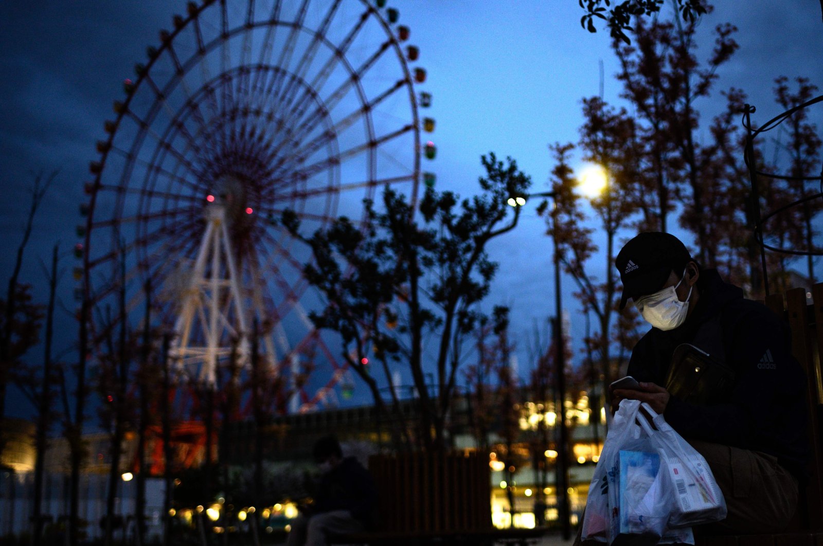 A man wearing a face mask looks at his mobile phone before a ferris wheel in the Odaiba area in Tokyo, April 19, 2020. (AFP Photo)