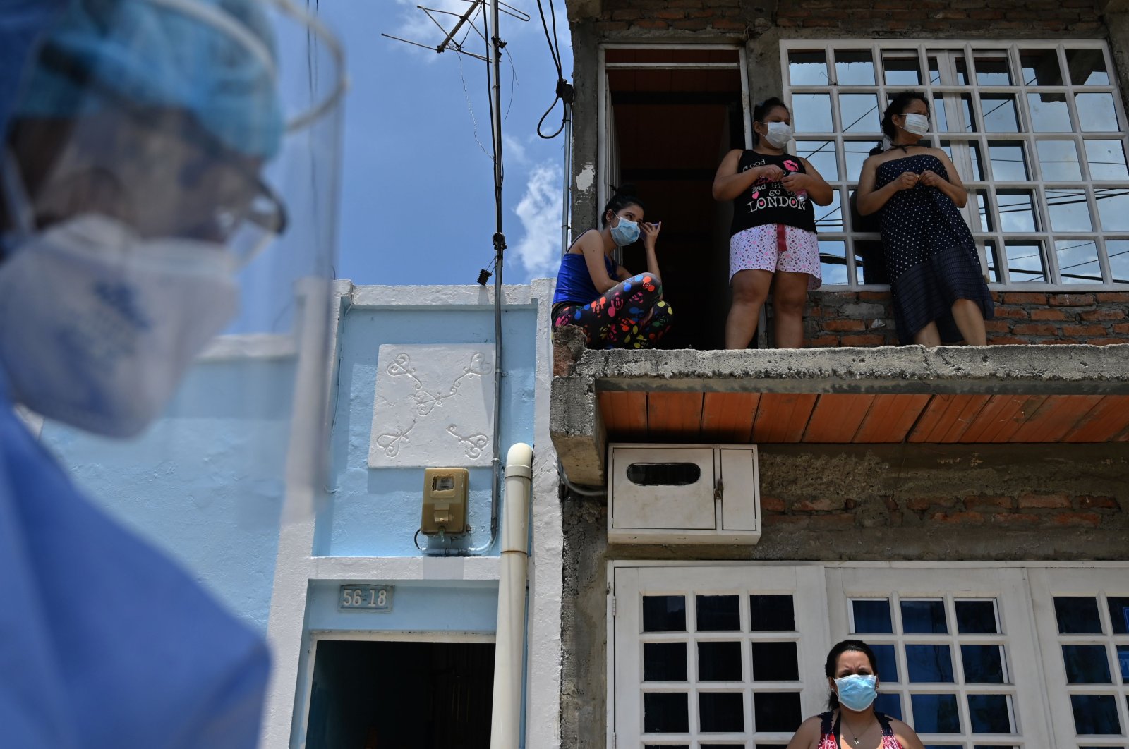 Locals look out from their house as health workers wearing biosafety suits carry out a checkup for the coronavirus at Nueva Floresta neighborhood in Cali, Colombia, on April 20, 2020.  (AFP)