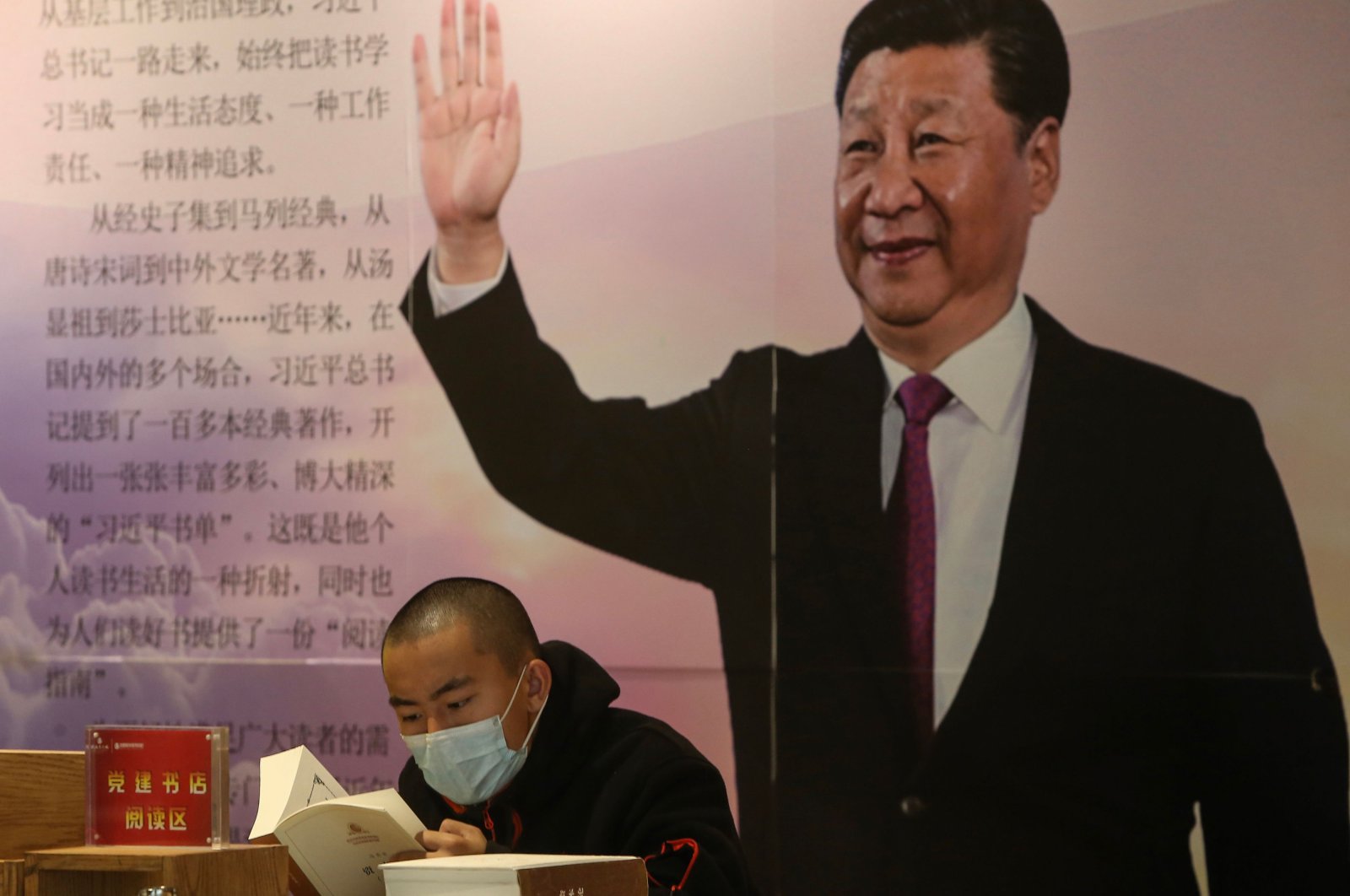 A man reads a book in front of a board with an image of China's President Xi Jinping at a book store during World Book Day in Shenyang in China's northeastern Liaoning province on April 23, 2020. (AFP Photo)