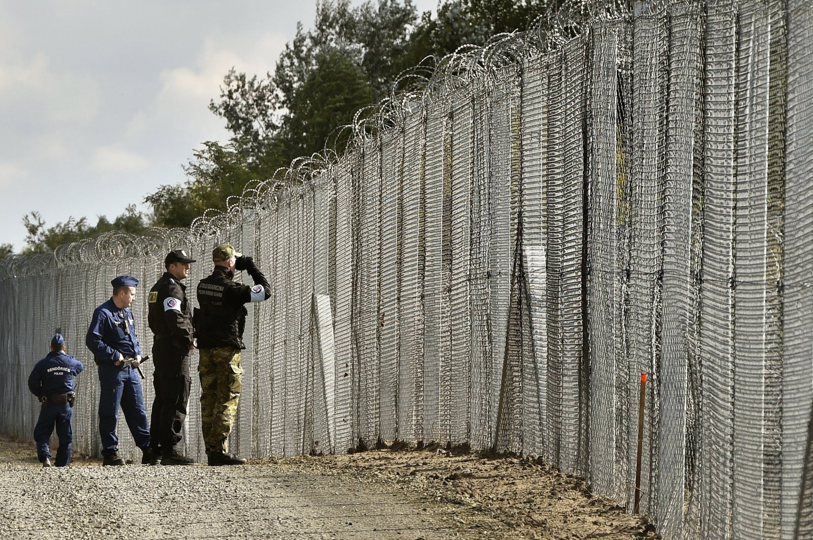 A police officer, second right, and border guard, right, of Poland patrol with Hungarian policemen along the temporary border fence on the Hungarian-Serbian border near Roszke, 180 kms southeast of Budapest, Oct. 13, 2016. (AP Photo)