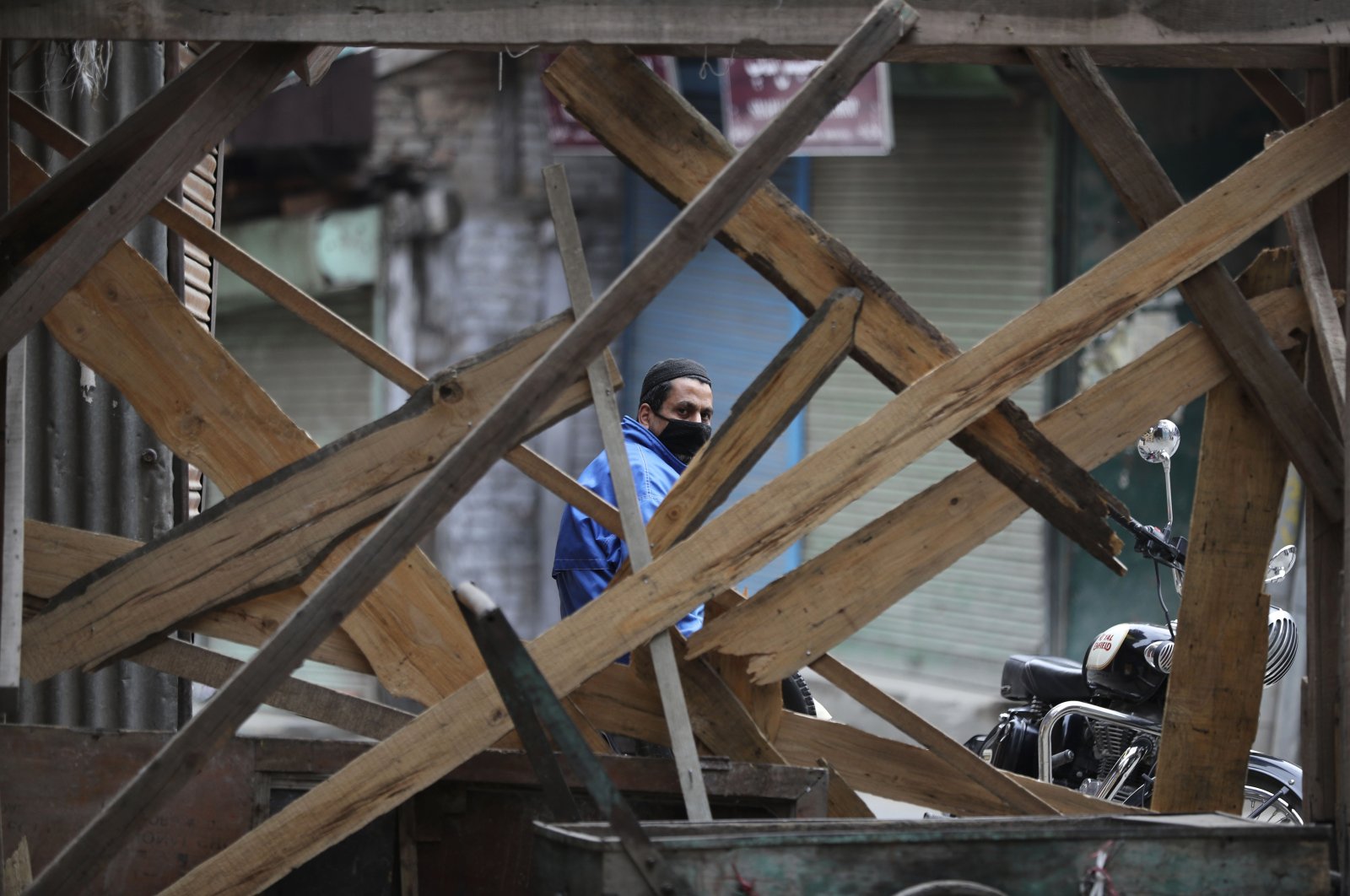 A Kashmiri volunteer looks through temporary barricades erected to prevent outsiders from entering an area declared as red zone by the government during lockdown in Srinagar, Indian controlled Kashmir, Tuesday, April 14, 2020. (AP Photo)