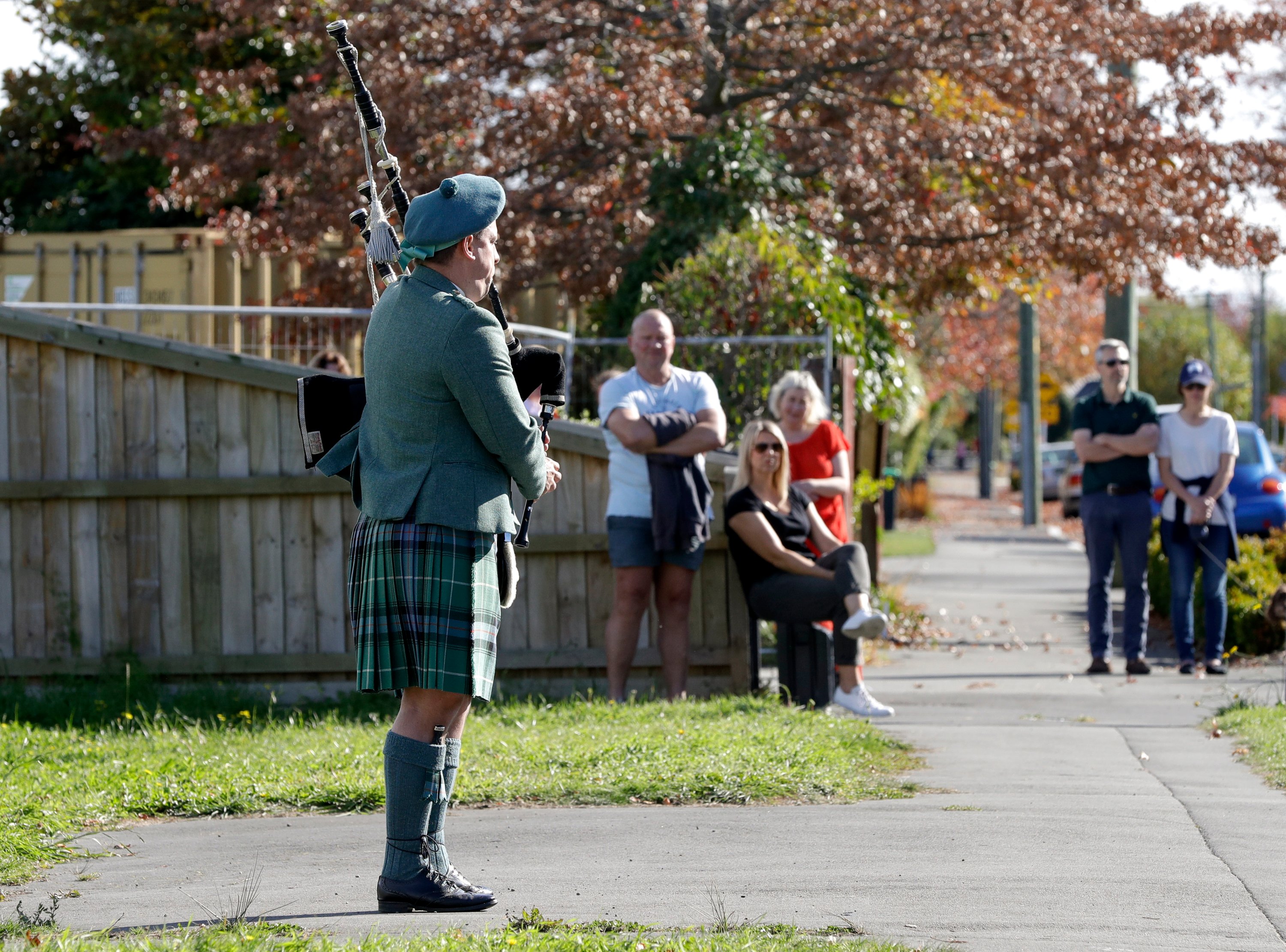 Neighbors watch as Tom Glover plays the bagpipes to commemorate Anzac Day in a suburb of Christchurch, New Zealand, Saturday, April 25, 2020. (AP Photo)