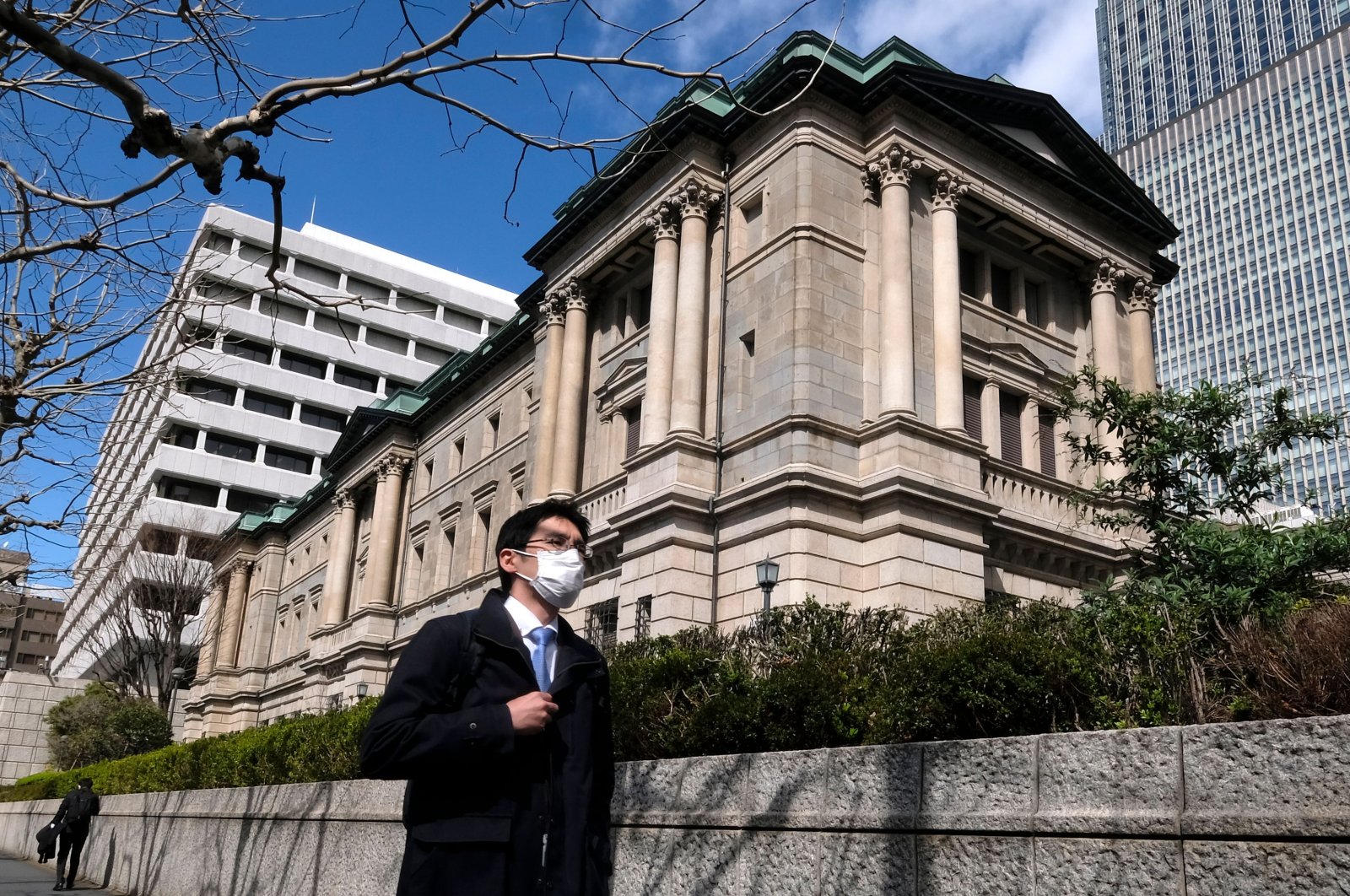A pedestrian wearing a face mask walks in front of the Bank of Japan headquarters in Tokyo, March 16, 2020. (AFP Photo)