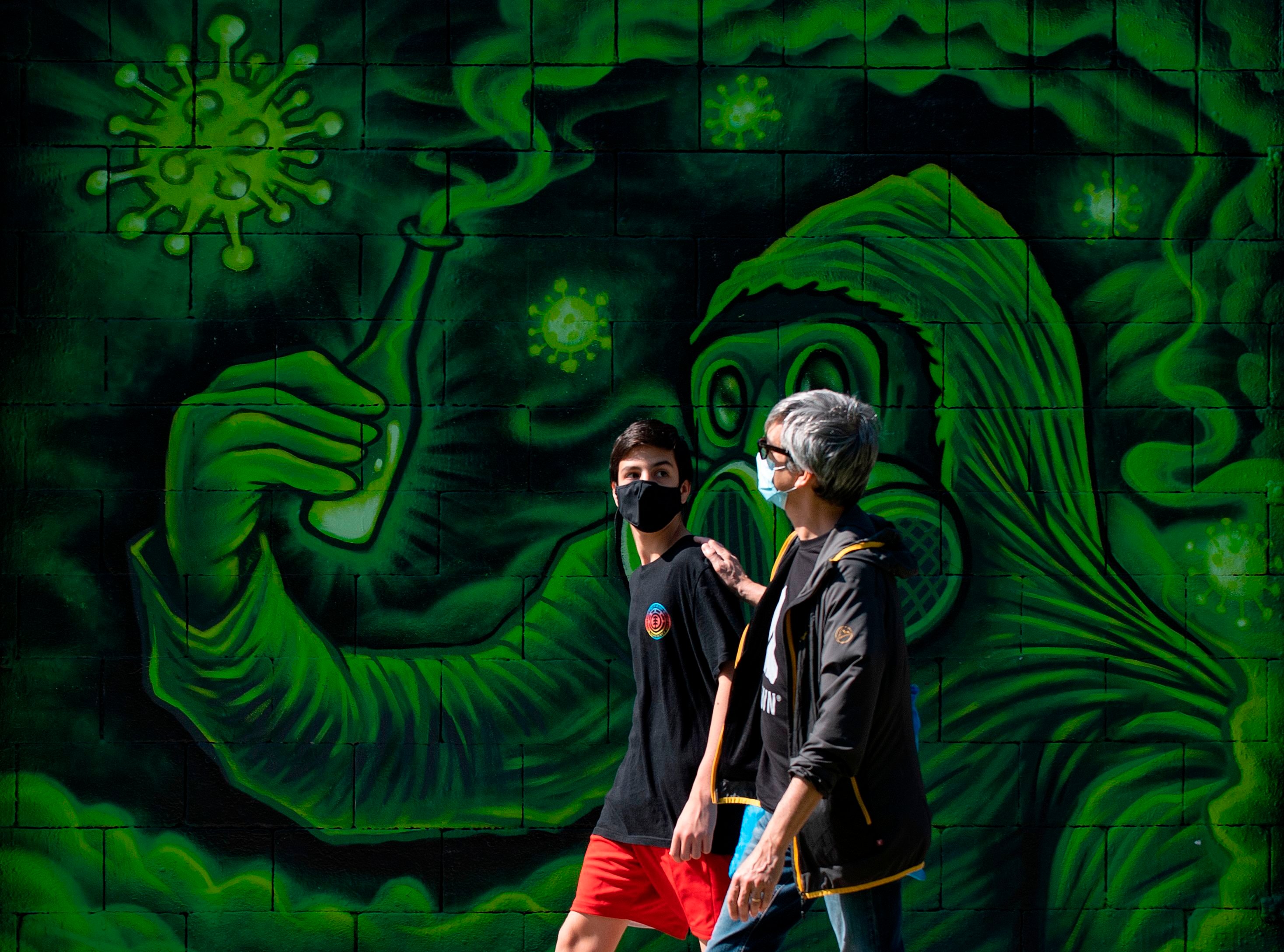 A man and a boy wearing face masks walk past graffiti inspired by COVID-19 in Barcelona, April 26, 2020. (AFP Photo)