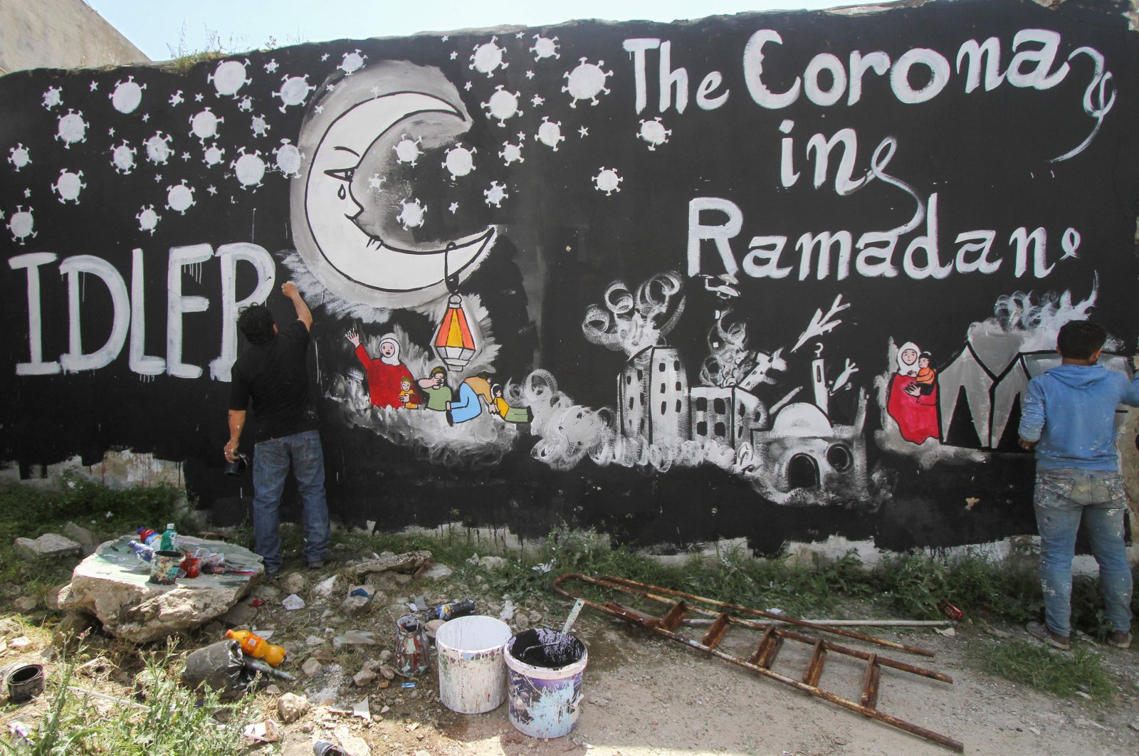 Syrian artist Aziz al-Asmar and his assistant Bachar Hamdoun paint a mural depicting the situation of displaced Syrians in camps amid the COVID-19 pandemic ahead of the holy fasting month of Ramadan, in the town of Binnish in Syria's northwestern Idlib province on April 23, 2020. (AFP Photo)