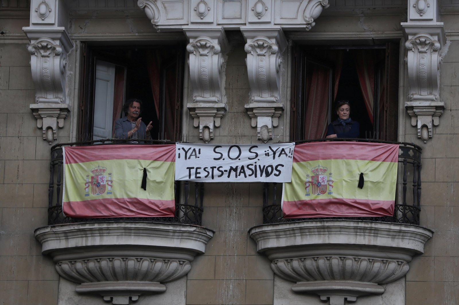 People react from their balconies next to Spanish flags with black ribbons and a banner during the daily applause for in honour of healthcare workers, amid the coronavirus disease (COVID-19) outbreak, in Madrid, Spain, April 27, 2020. (Reuters Photo)