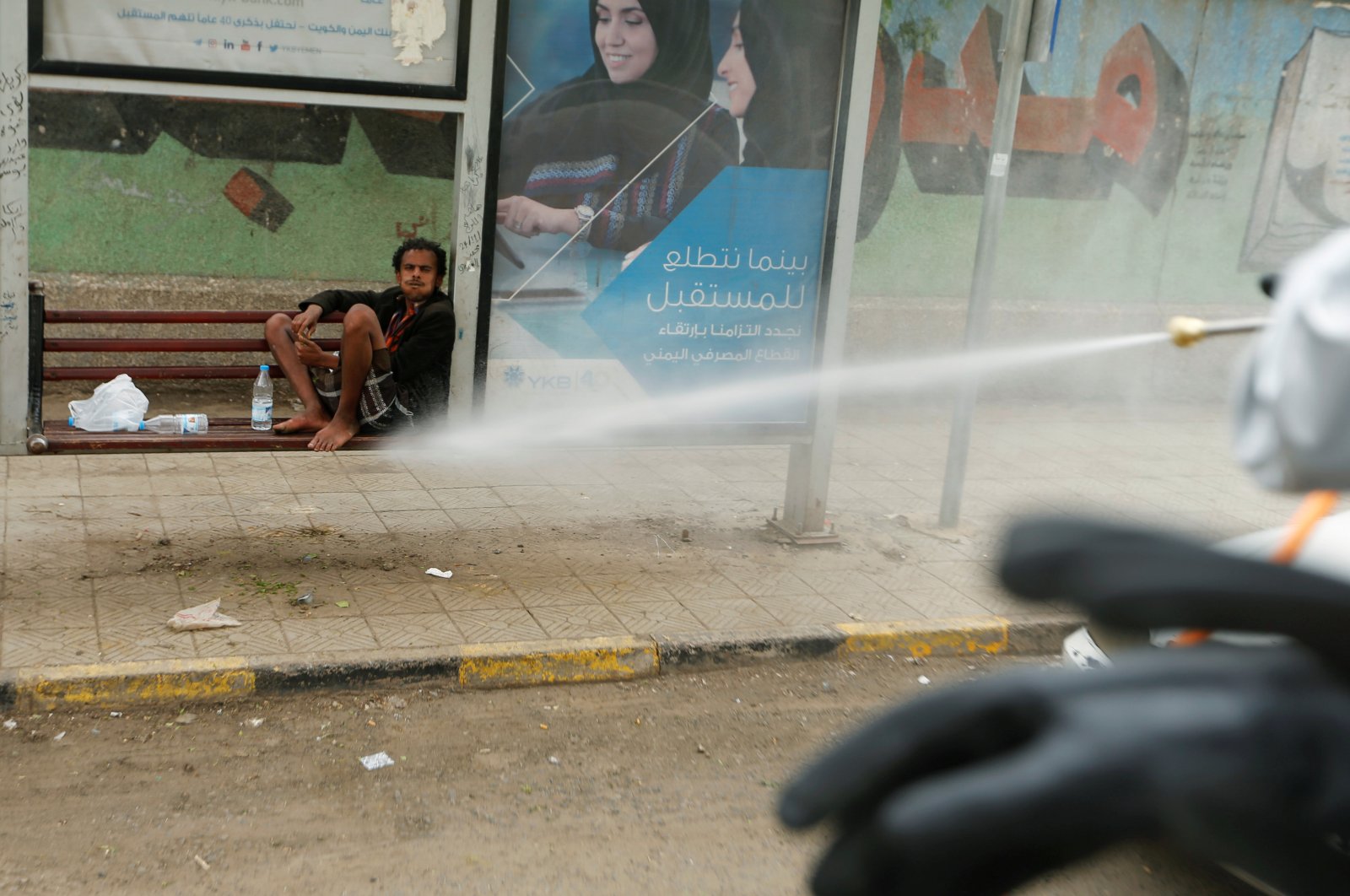 A man sits in an ad frame as health workers disinfect a street amid concerns of the spread of the coronavirus disease, Sanaa, April 28, 2020. (REUTERS Photo)