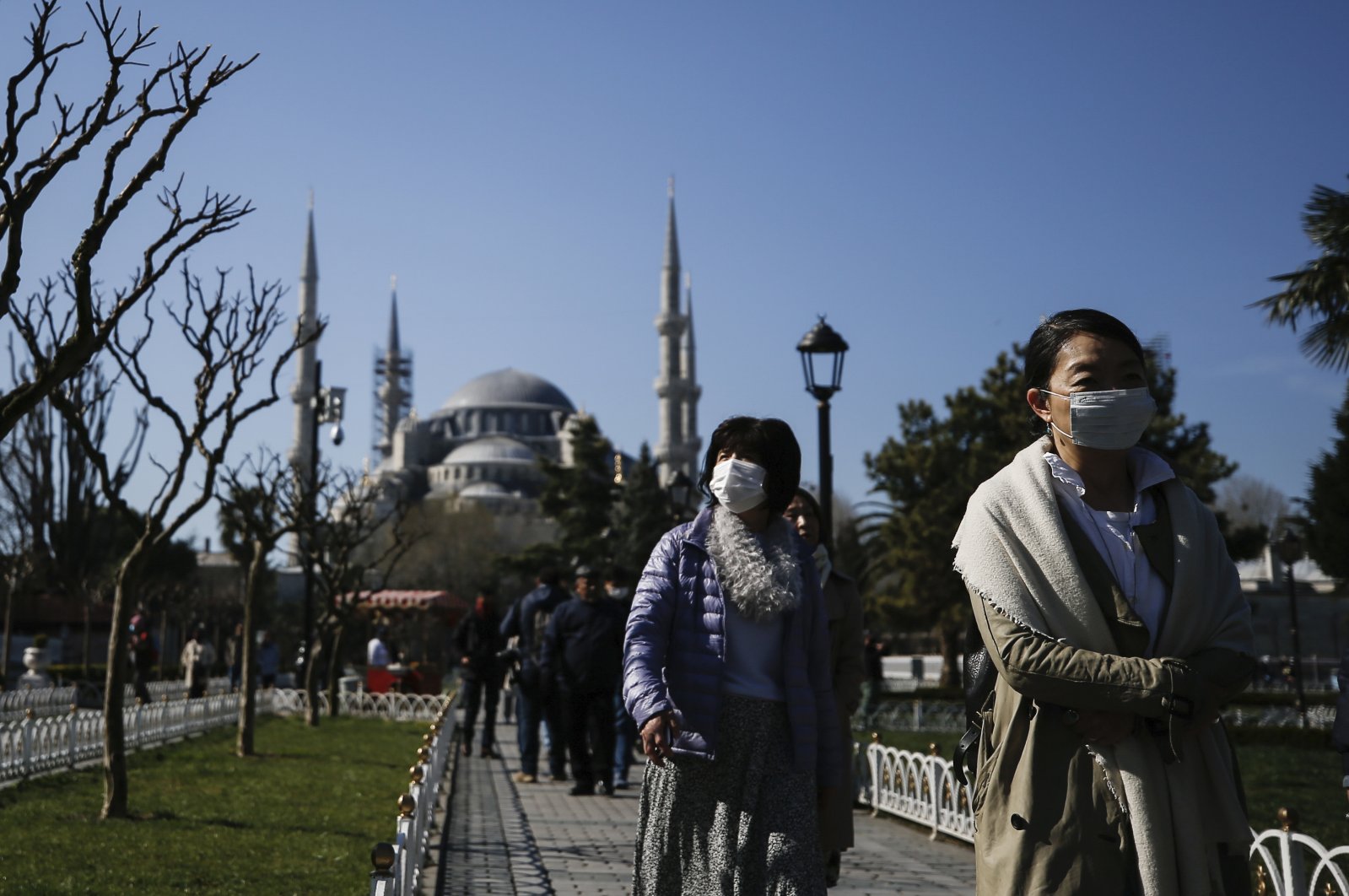 Tourists walk as municipality workers wearing face masks and protective suits disinfect the area surrounding the historical Blue Mosque, amid the coronavirus outbreak, in Istanbul, Turkey, March 21, 2020. (AP Photo)