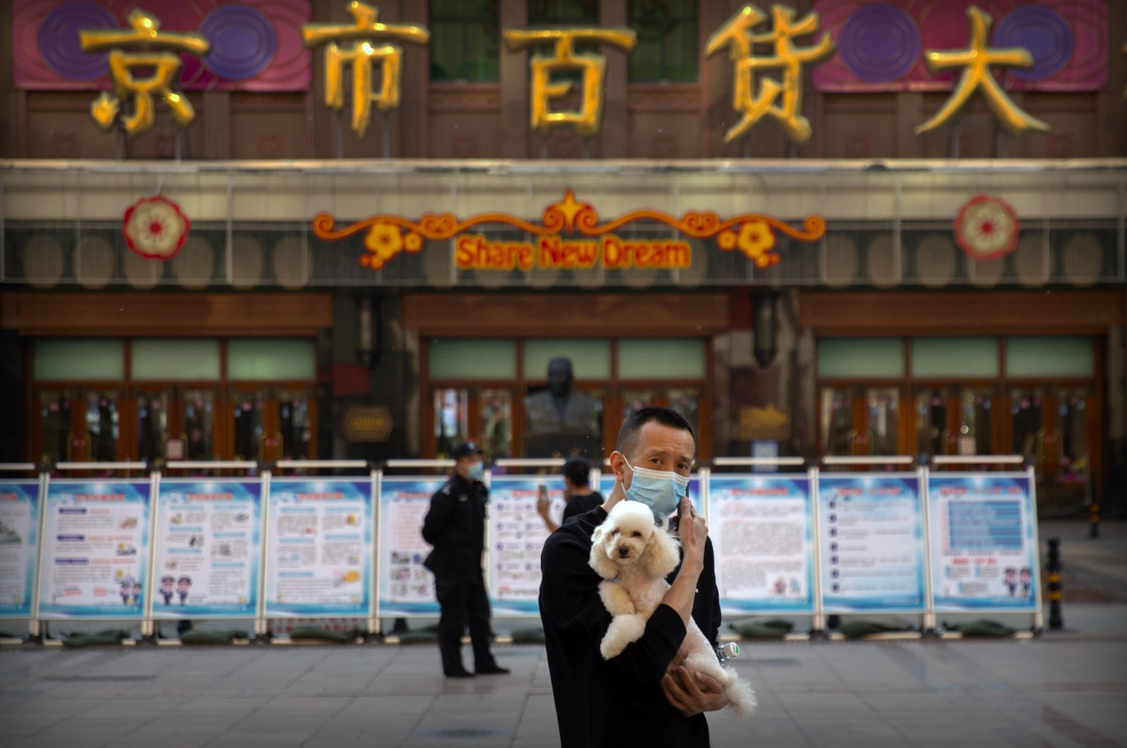 A man wearing a face mask to prevent the spread of the new coronavirus holds a dog as he stands along a pedestrian shopping street in Beijing, Tuesday, April 28, 2020. (AP Photo)