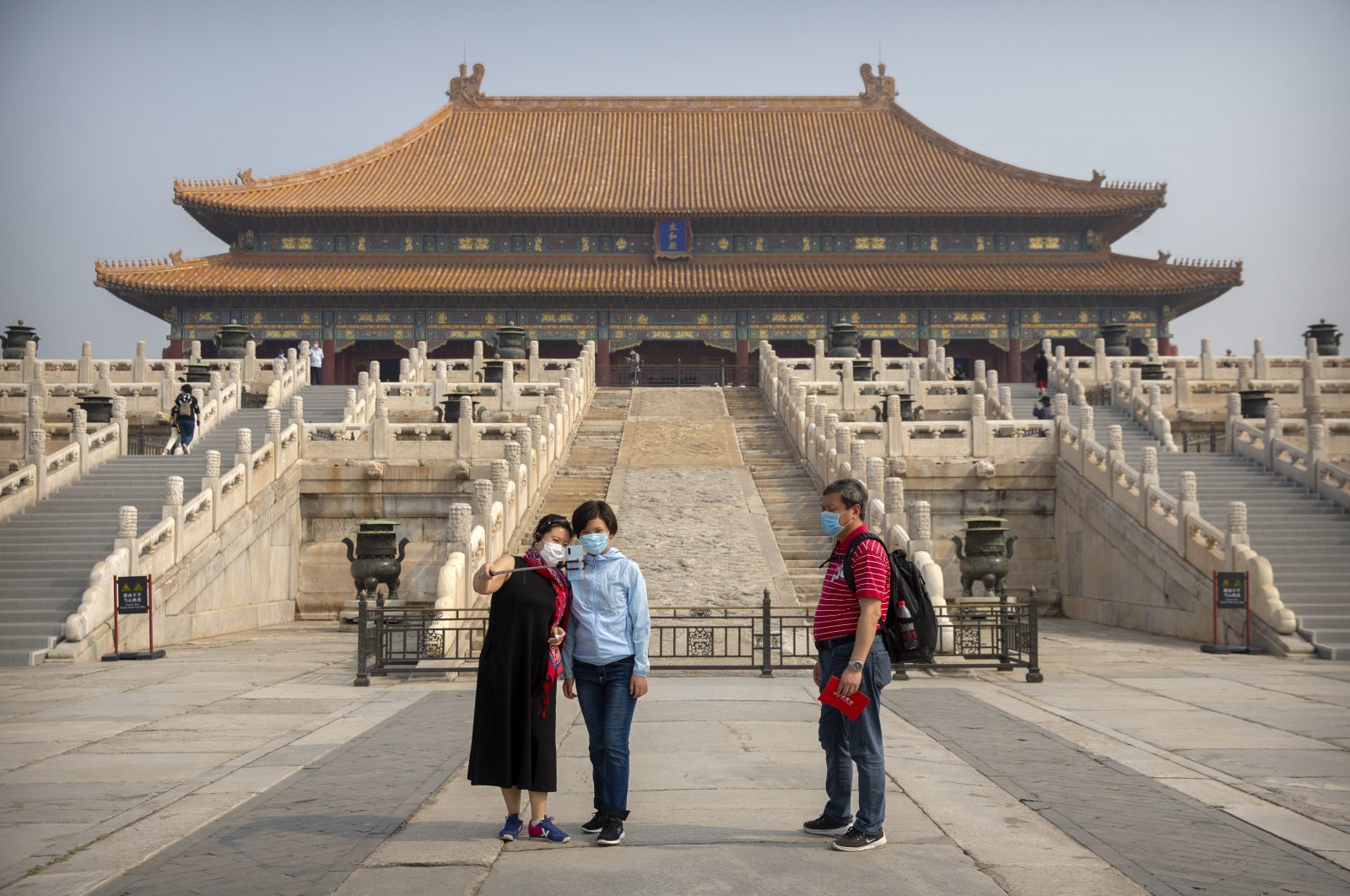 Visitors wearing face masks to protect against the new coronavirus pose for a selfie in the Forbidden City in Beijing, May 1, 2020. (AP Photo)