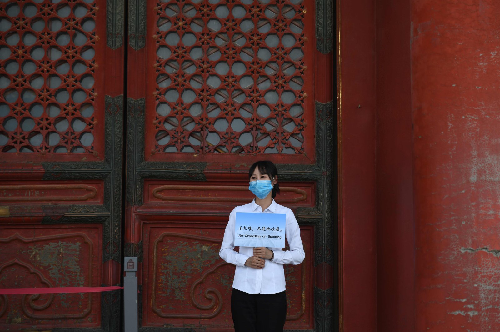An staff member wears a face mask as a preventive measure against the COVID-19 coronavirus as she holds a "No crowding or spitting" sign in the Forbidden City, the former palace of China's emperors, in Beijing on May 1, 2020. (AFP Photo)