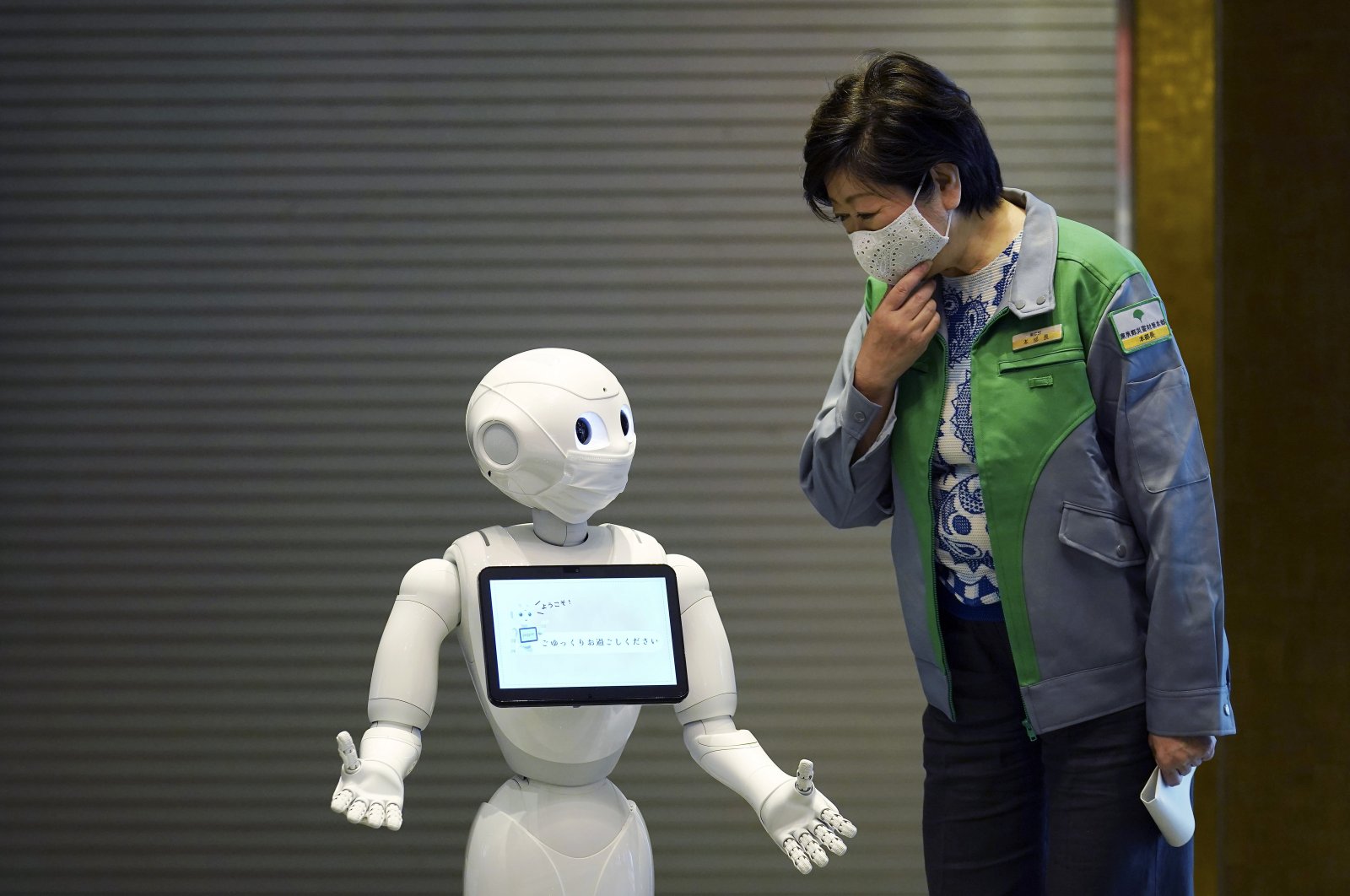 A humanoid robot Pepper wearing a face mask greets Tokyo Gov. Yuriko Koike at the lobby of a hotel for COVID-19 patients with mild symptoms during a media preview in Tokyo, Japan, Friday, May 1, 2020. (AP Photo)