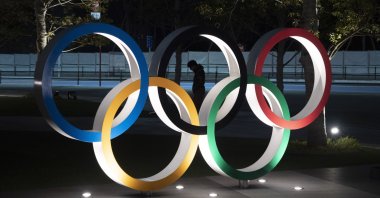 A man is seen through the Olympic rings in front of the New National Stadium in Tokyo, Japan on Tuesday, March 24, 2020. (AP Photo)