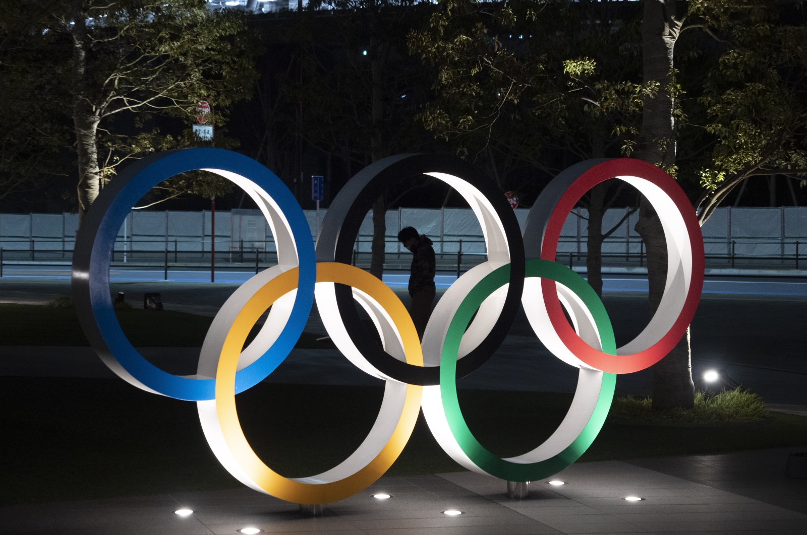 A man is seen through the Olympic rings in front of the New National Stadium in Tokyo, Japan on Tuesday, March 24, 2020. (AP Photo)