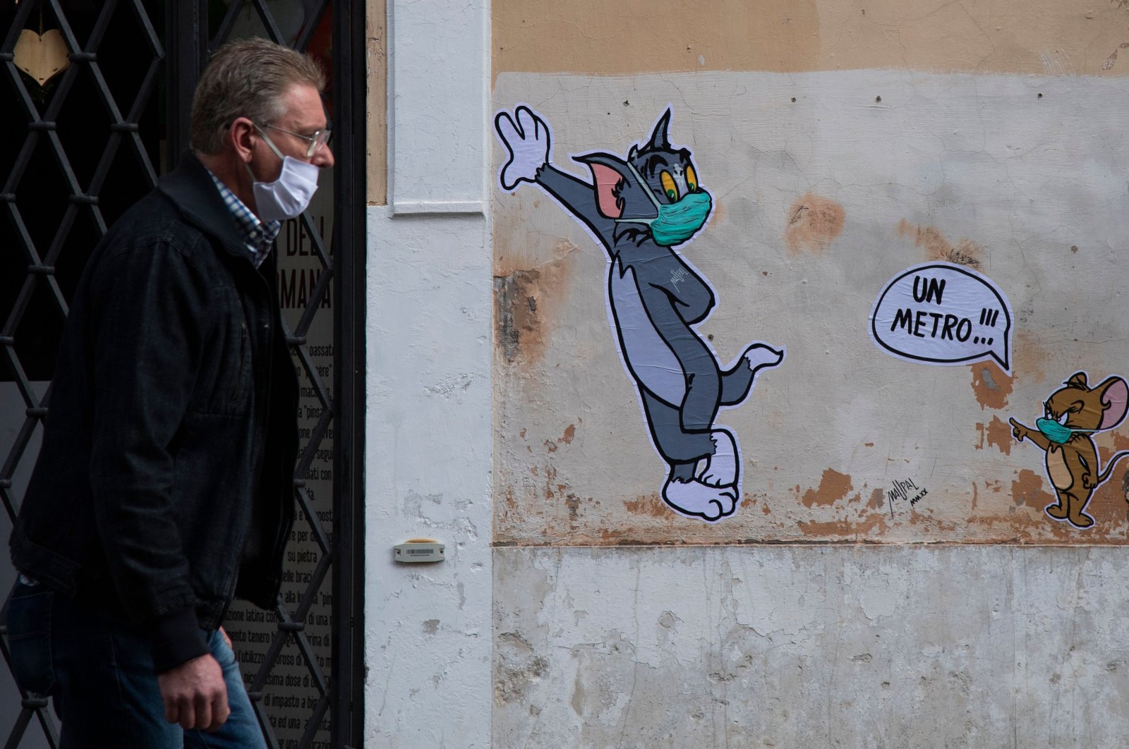 A man wearing a face mask walks past a mural by street artist Maupal, created to pay homage to late Gene Deitch, the creator of "Tom and Jerry," during the country's lockdown aimed at curbing the coronavirus spread, Rome, April 29, 2020. (AFP Photo)