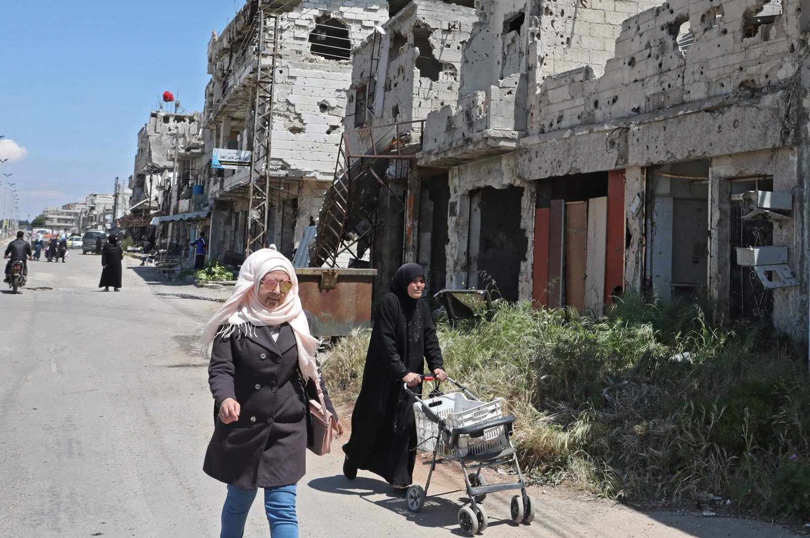Syrians walk past buildings heavily damaged during Syria's civil war, in the central city of Homs, April 28, 2020. (AFP)