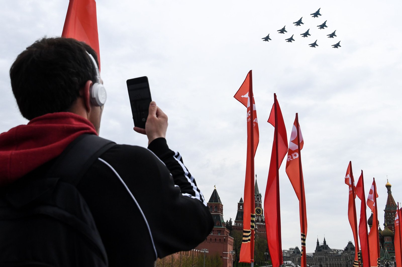 A man takes pictures with his mobile phone of Russian Su-34 fighter bombers, Su-30M jet fighters and Su-35 jet fighters flying over the Red Square during a rehearsal for the Victory Day military parade in Moscow on May 4, 2020. (AFP Photo)