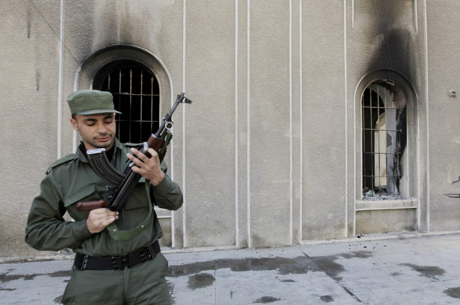 A Syrian regime soldier checks his AK-47 as he stands in front the burned court building that was set on fire by anti-regime protesters, in the southern city of Daraa, Syria, March 21, 2011. (AP Photo)
