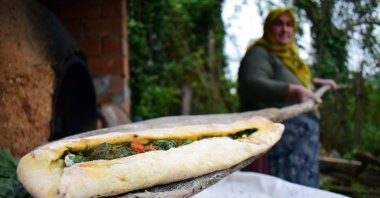 A woman takes a pide filled with collard greens from an earthen oven, in Çayağzı village, Düzce province, Turkey, April 26, 2020. (AA Photo)