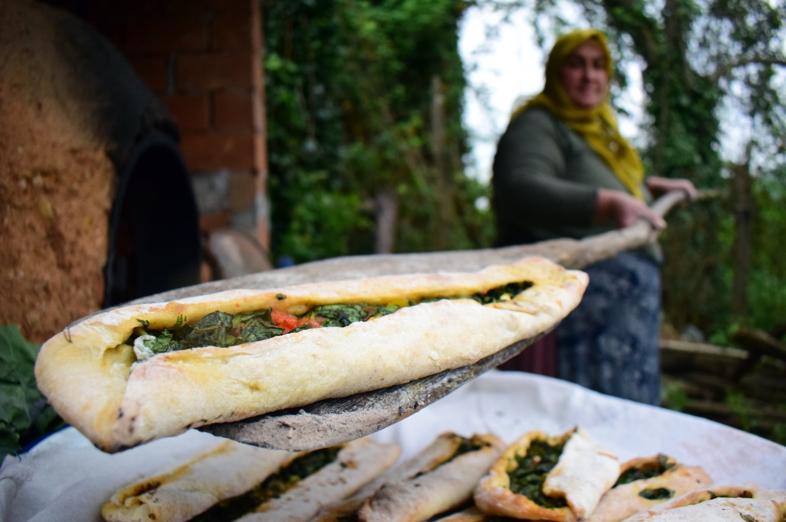 A woman takes a pide filled with collard greens from an earthen oven, in Çayağzı village, Düzce province, Turkey, April 26, 2020. (AA Photo)