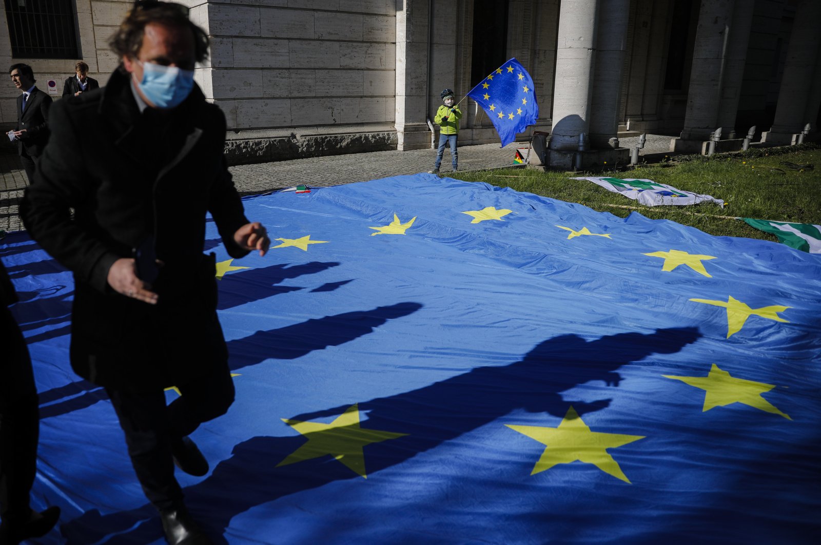 A man with a face mask and a child with a European flag attend an event of the Pulse of Europe movement to collect signatures for more support for Italy during the coronavirus outbreak in front of the Italian embassy in Berlin, Germany, April 22, 2020. (AP Photo)