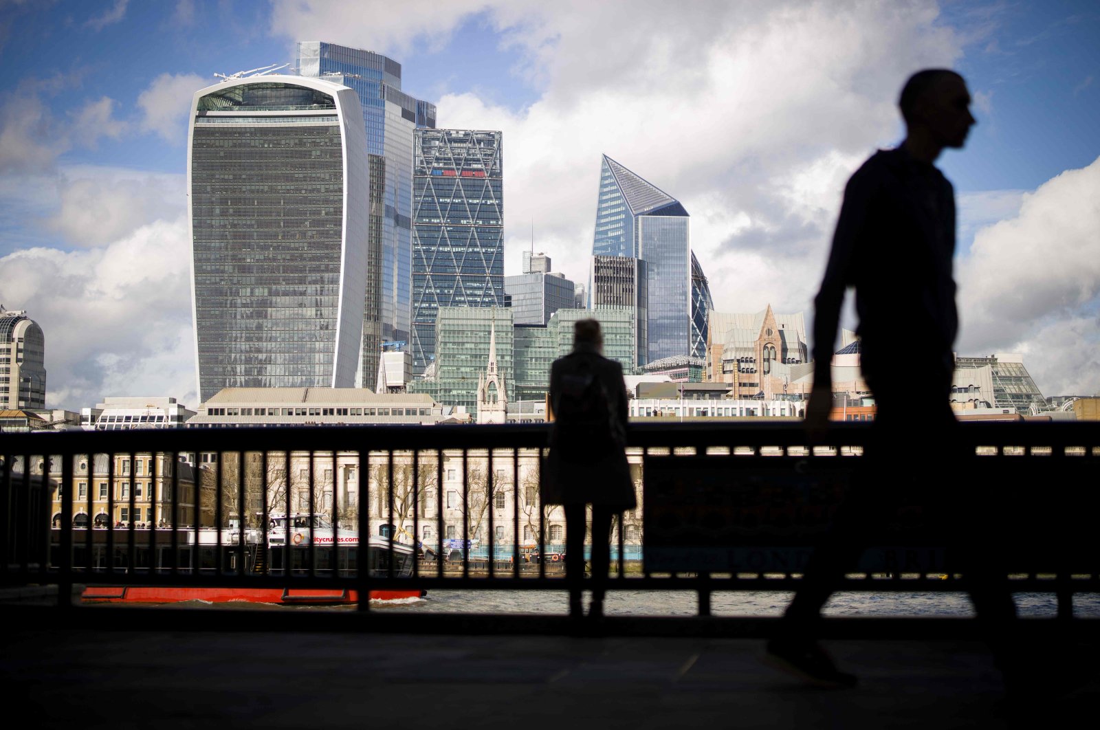 Pedestrians walk by with the towers of the City of London in the background in London, March 11, 2020. (AFP Photo)