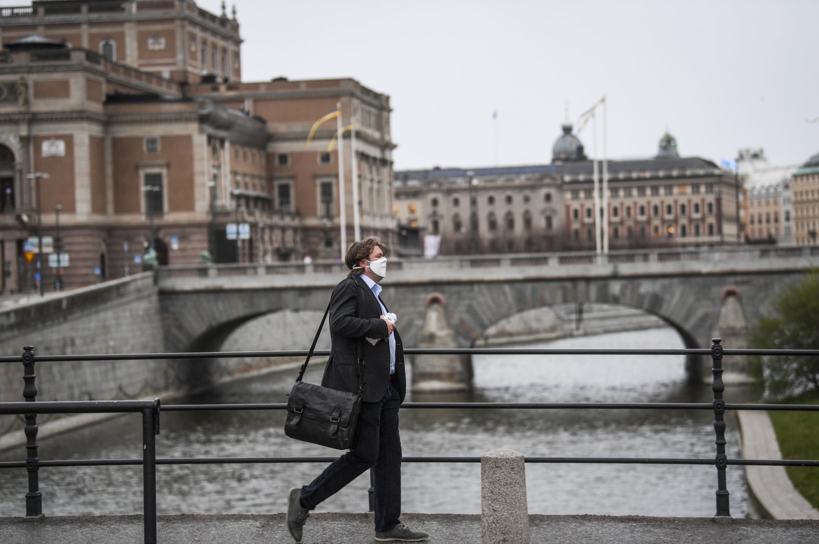 A man wearing a protective mask walks in the rain past the Royal Swedish Opera (at left) in Stockholm, Sweden, 27 April 2020, amid the coronavirus disease (COVID-19) outbreak.  (EPA-EFE Photo)