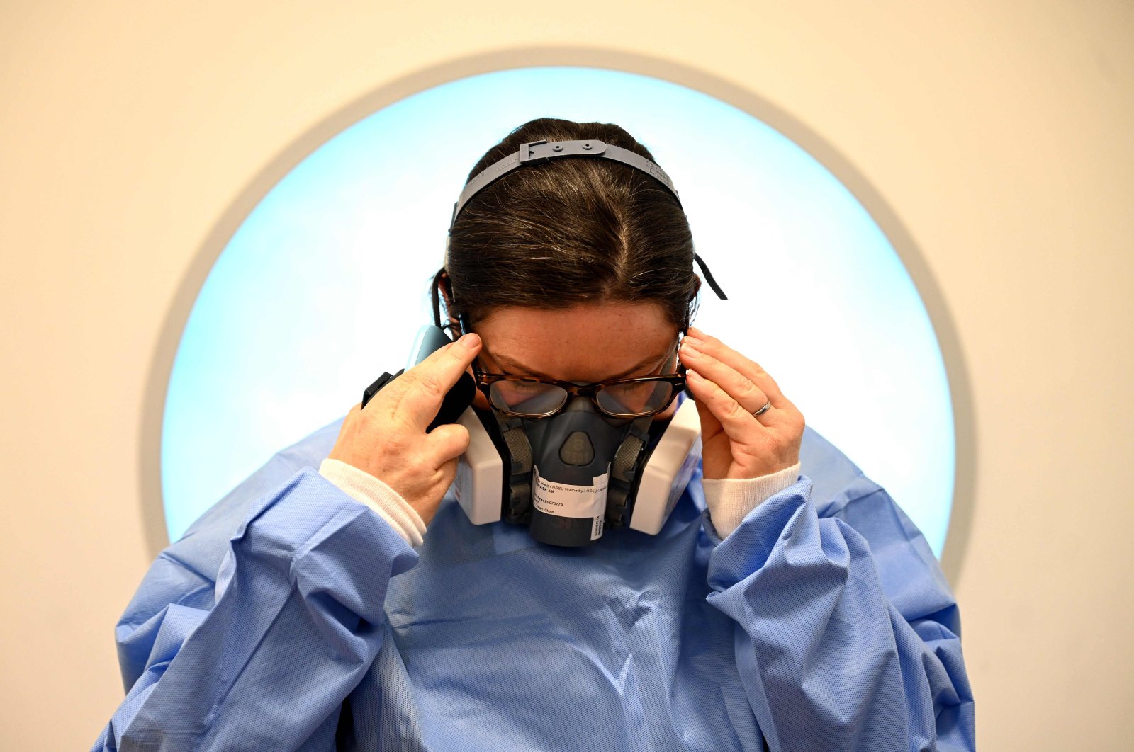 A member of the clinical staff adjusts her glasses as she dons personal protective equipment (PPE) including a mask and gown at the Intensive Care unit at Royal Papworth Hospital in Cambridge, on May 5, 2020. (AFP File Photo)