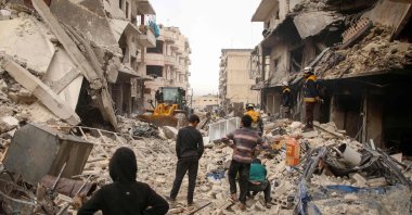 Members of the Syrian Civil Defence, also known as the White Helmets, watch as a bulldozer clears rubble and debris at the site of reported airstrikes on the town of Ariha in the northern countryside of Syria's Idlib province, Jan. 30, 2020. (AFP Photo)
