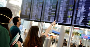 People wearing protective face masks in light of the coronavirus outbreak look at flight status information at Istanbul Airport, Turkey, March 13, 2020. (Reuters Photo)