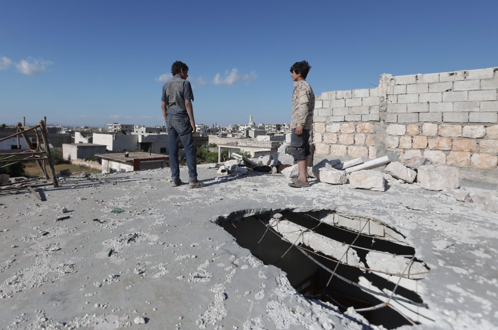 Syrian youths stand on May 6, 2020 on the damaged roof of a building in al-Nayrab, a town ravaged by pro-Assad forces' bombardment near the M4 strategic highway, in Syria's northwestern Idlib province (AFP Photo)