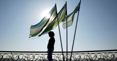 A girl is silhouetted against the sun standing next to Uzbek flags in Tashkent. (Reuters Photo)