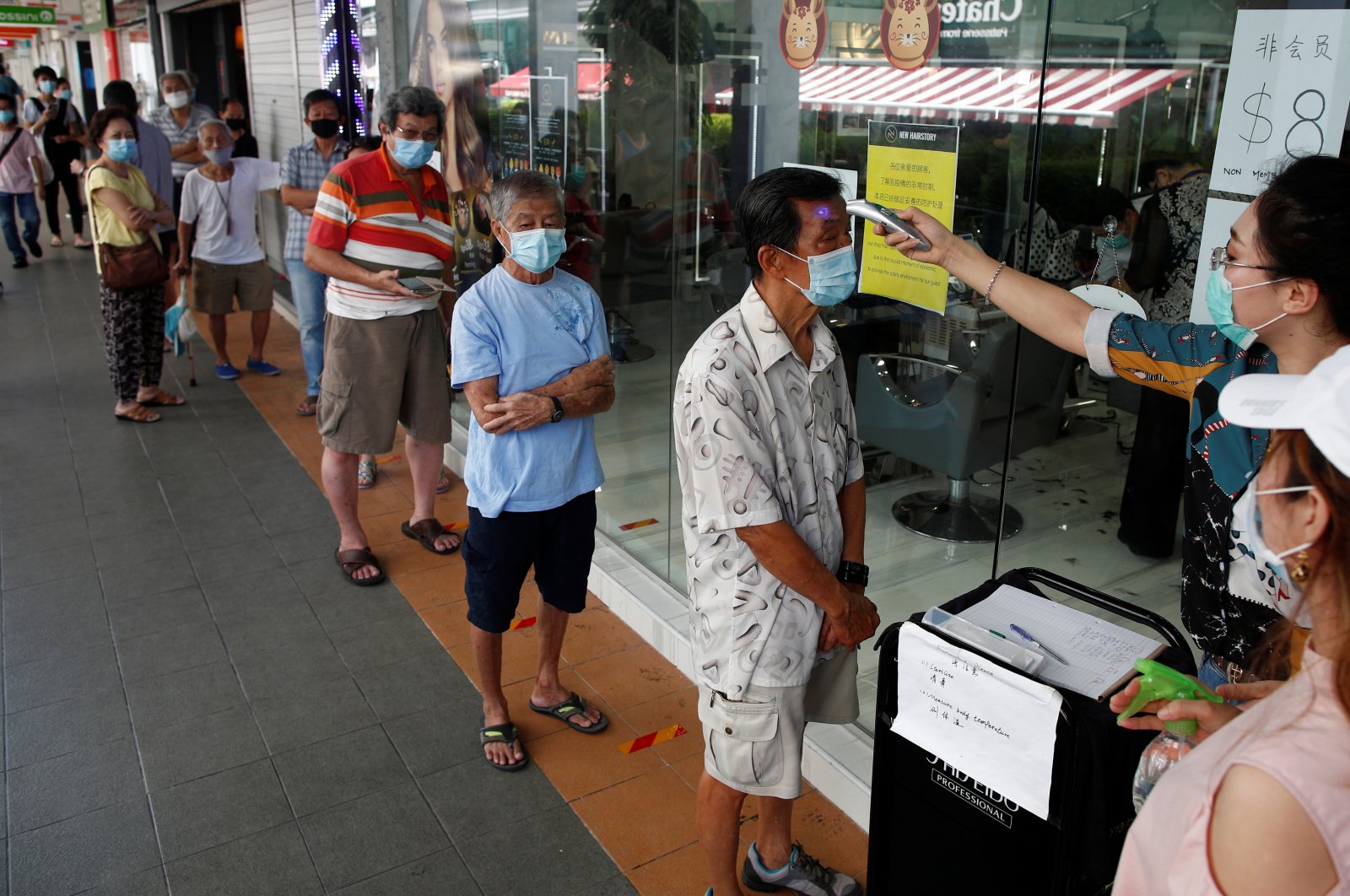 Customers queue up to have their temperature taken outside a hairdressing salon as they reopen for business amid the coronavirus disease (COVID-19) outbreak in Singapore May 12, 2020. (Reuters Photo)