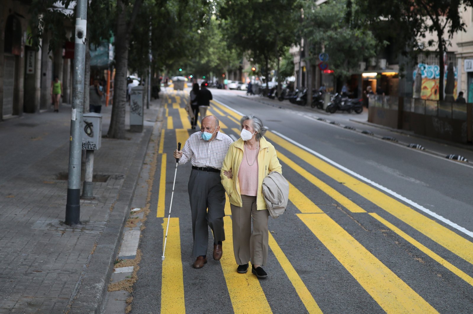 An elderly couple wearing face masks walks on a sidewalk marked for pedestrians to keep social distance, Barcelona, May 11, 2020. (REUTERS Photo)