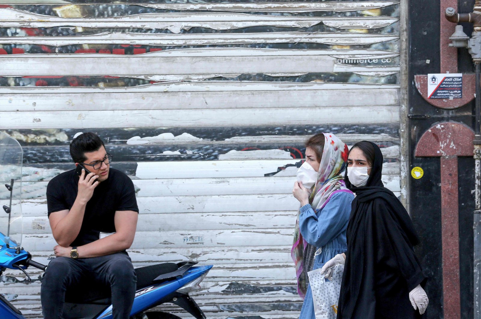 An Iranian youth talks on the phone as he watches women wearing protective masks walk by on a street of the capital Tehran, May 9, 2020. (AFP)