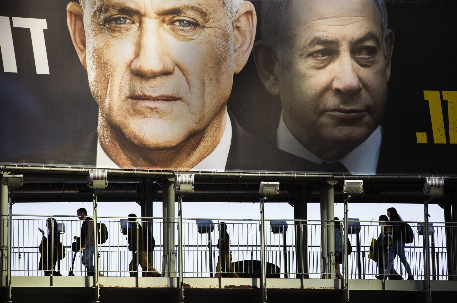 People walk on a bridge under an election campaign billboard for the Blue and White party, then an opposition party led by Benny Gantz, left, and showing Israeli Prime Minister Benjamin Netanyahu, Ramat Gan, Israel, Feb. 18, 2020. (AP Photo)