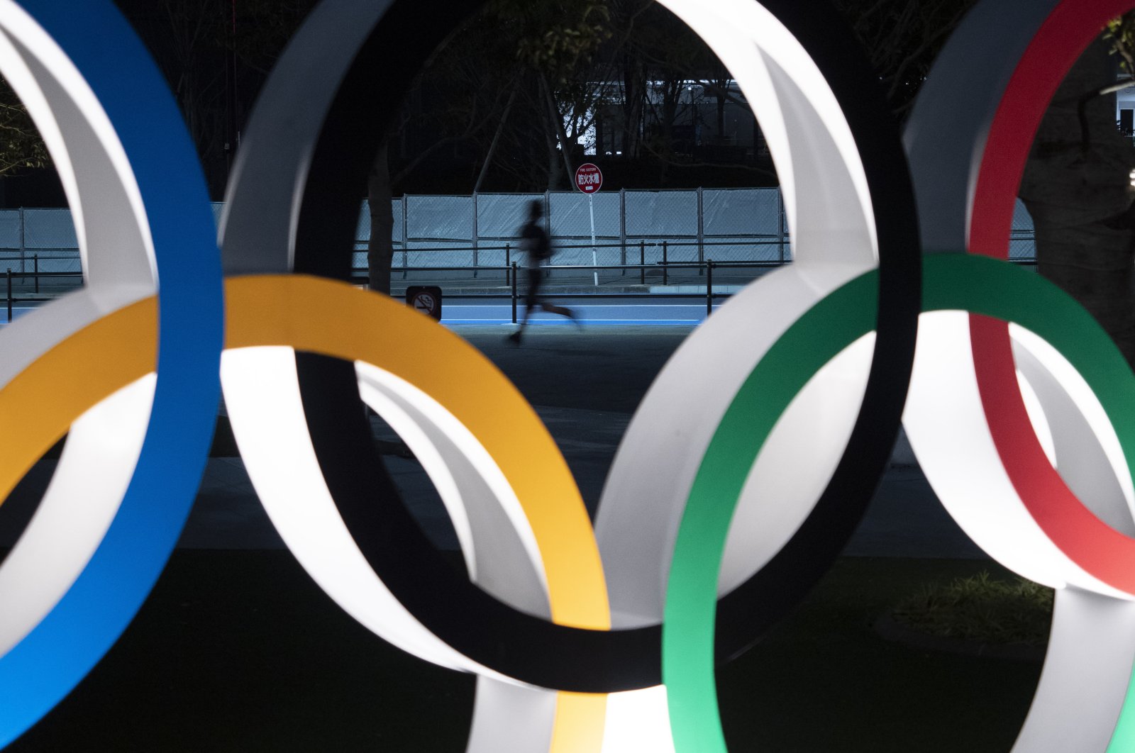 A man jogs past the Olympic rings in Tokyo, March 30, 2020. (AP Photo)