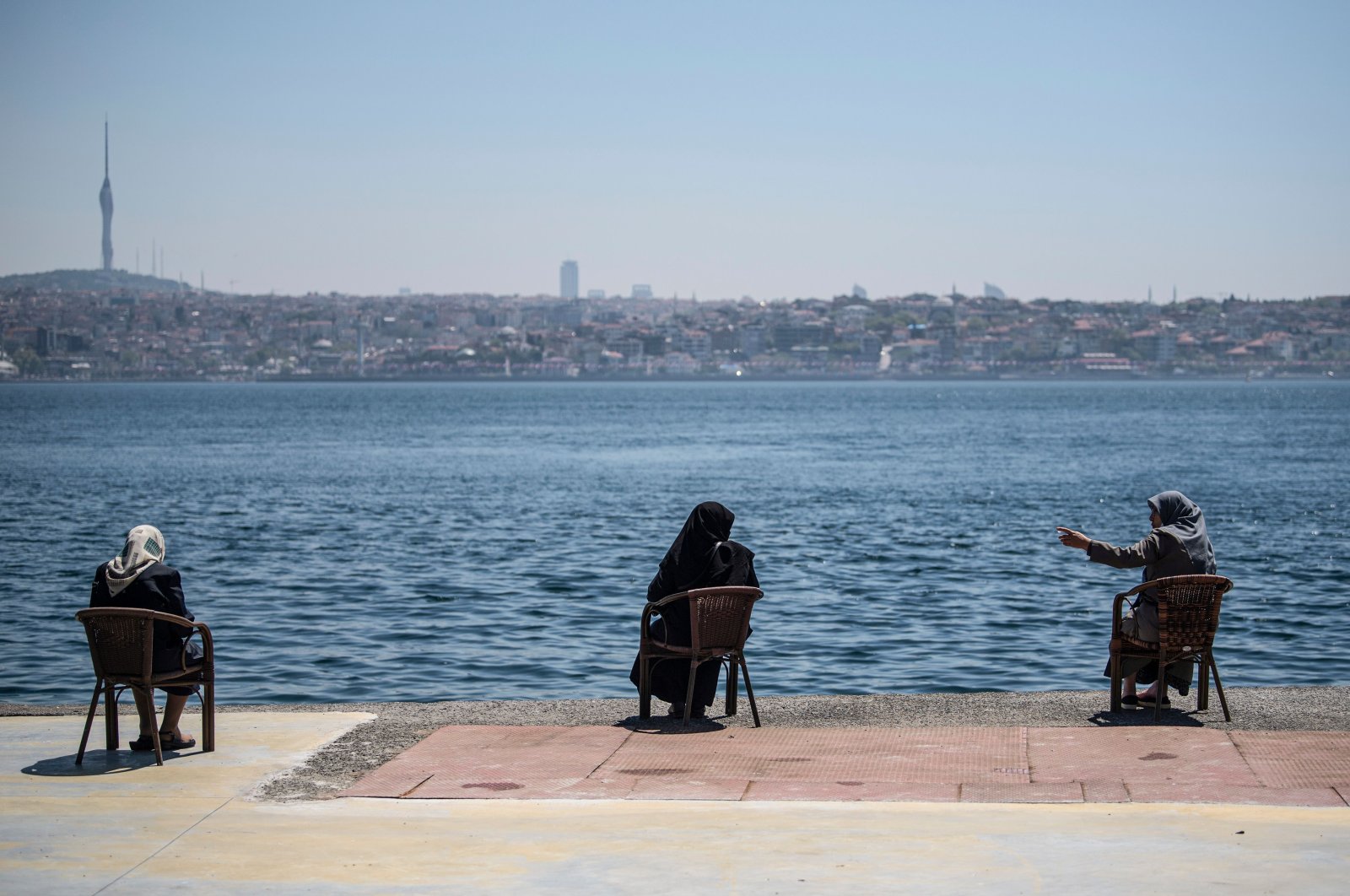 Women wearing protective face masks sit apart following social distancing measures at the seaside overlooking the Bosporus in Istanbul, Turkey, May 10, 2020. (AP Photo)