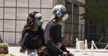 A couple wearing protective masks from the coronavirus ride a scooter down the street past the Ronald Reagan UCLA Medical Center in the Westwood section of Los Angeles, California, U.S. on May 15, 2020. (AP Photo)