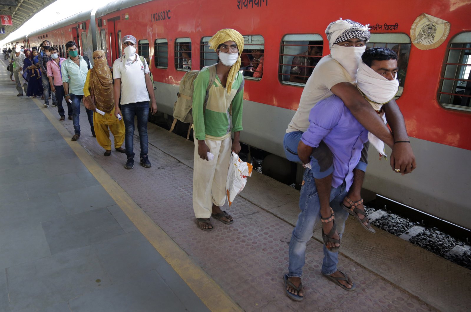 In this Saturday, May 2, 2020, photo, a man carries his physically disabled brother on his back as they wait to board a special train to return to Agra in Uttar Pradesh state, during a nationwide lockdown to curb the spread of new coronavirus, at a railway station in Ahmedabad, in the western Indian state of Gujarat. (AP Photo)